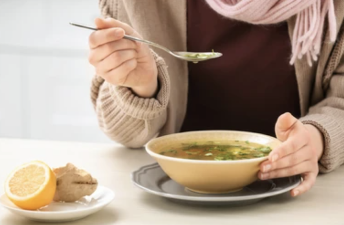 immune-boosting foods for flu season woman eating soup with a scarf on